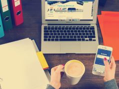 Osoba drži telefon pored šolje kafe i laptopa