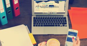 Osoba drži telefon pored šolje kafe i laptopa