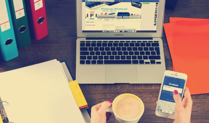 Osoba drži telefon pored šolje kafe i laptopa